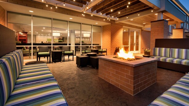 Un área de estar exterior con una chimenea, asientos acolchados y vista al interior.