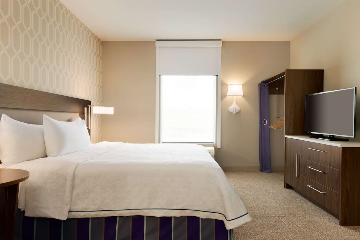 A hotel room with a large bed, a TV, a wardrobe, and a window with curtains.