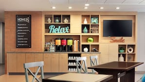 Un moderno vestíbulo de hotel con un mostrador de recepción de madera, un televisor de pantalla plana grande y un cartel que dice 'Home2 Guarantee'.