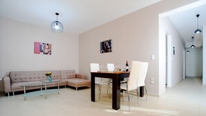 Un salon moderne comprenant un canapé, une table basse, une table à manger et des chaises. Les murs sont ornés de tableaux abstraits et le plafond est éclairé par un luminaire.