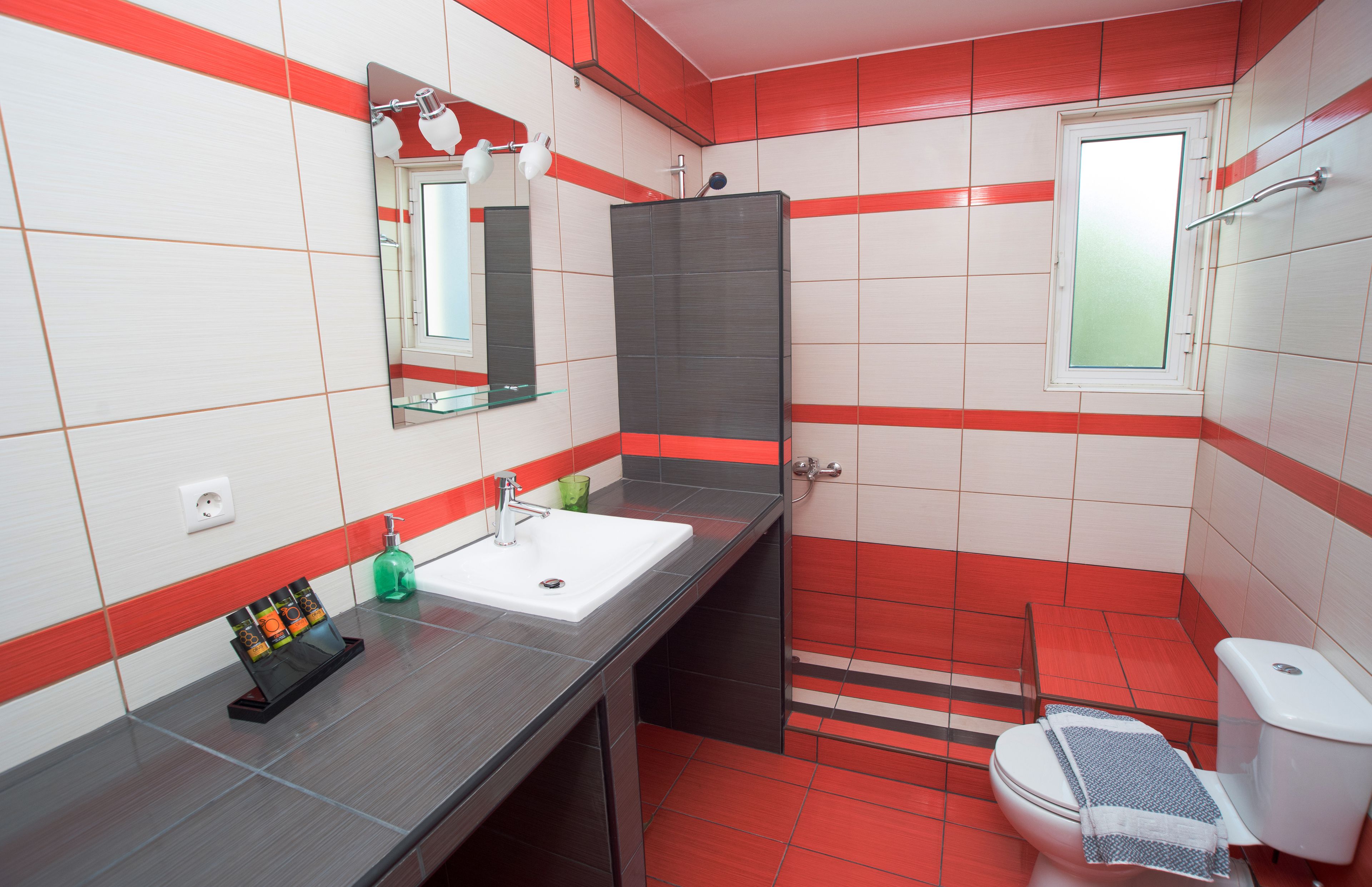 Een badkamer met een wit wastafelmeubel, spiegel en rode betegelde wanden.