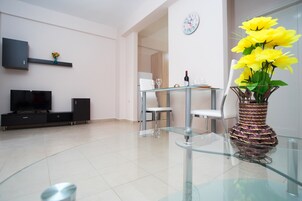 Una sala moderna con un televisor de pantalla plana, una mesa de centro de vidrio y un comedor con una mesa y sillas de vidrio.