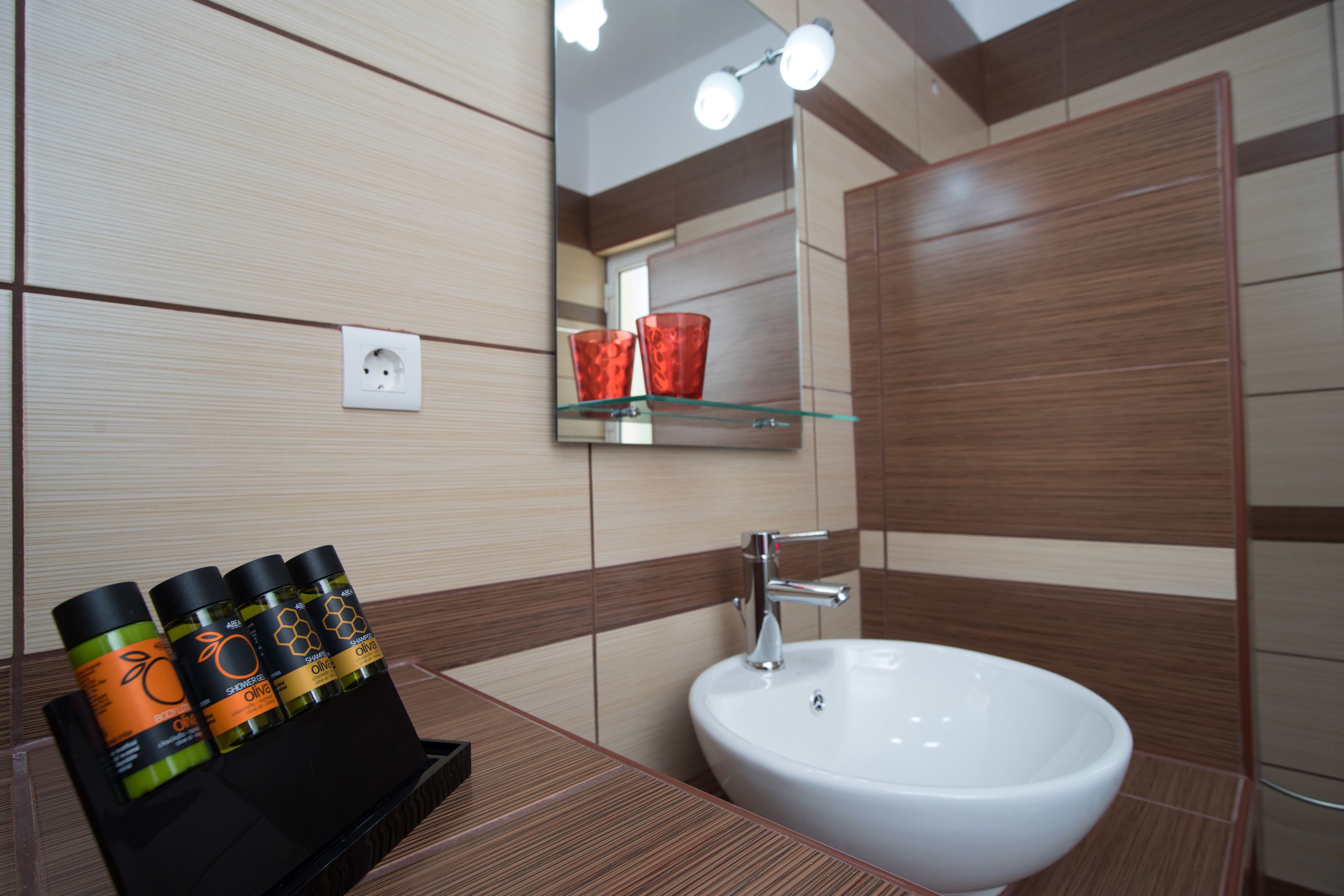 A bathroom with a white sink, a mirror, and a shelf with three bottles of olive oil.
