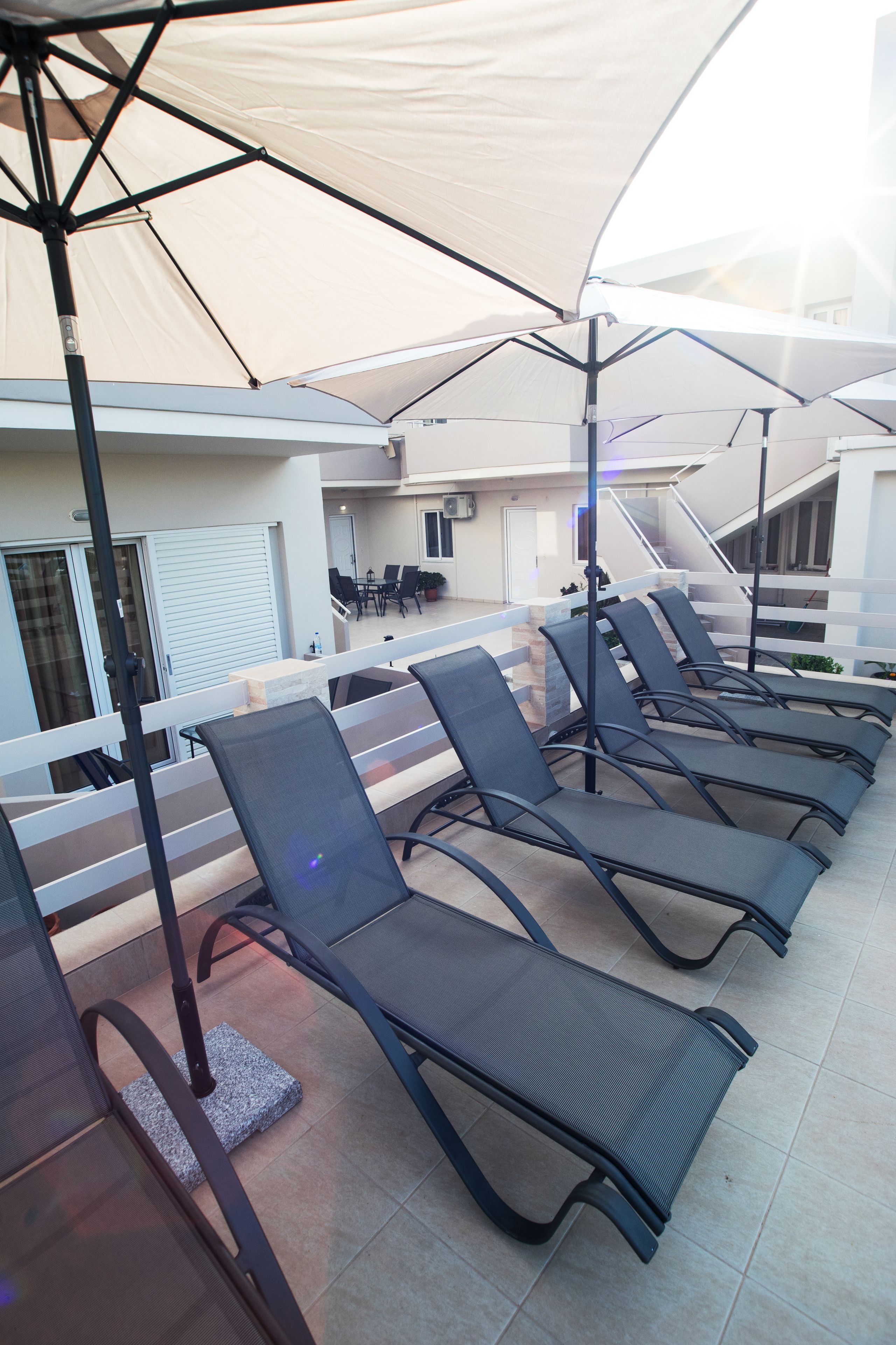 A rooftop terrace with sun loungers, a table, and chairs, featuring a view of the building's interior.