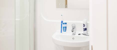 Een moderne badkamer met een douchecabine van glas, een wit wastafelmeubel en toiletartikelen op de wastafel.