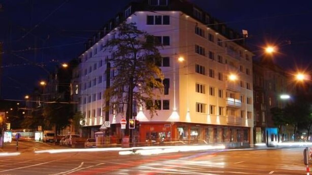 Een meerlaags hotel op een hoek, verlicht door straatverlichting en met een zichtbaar verkeerslicht.