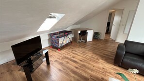Een modern loft appartement met een schuine kap, houten vloer, een zwarte leren bank, een televisie en een kleurrijke kinderwagen.
