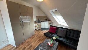 Een modern loft appartement met een kitchenette, een zwarte leren bank en een eettafel.