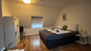 Een slaapkamer met een bed, een televisie, een raam, een lamp en een plank.