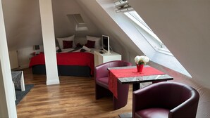 Een moderne loft slaapkamer met een schuine kap, een bed met rode beddengoed, een bureau met een lamp, en een tafeltje met een bloemenvaas.