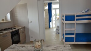 A modern kitchen with a gas stove, oven, and a small dining table with a glass vase. There is a bunk bed with blue bedding in the room.