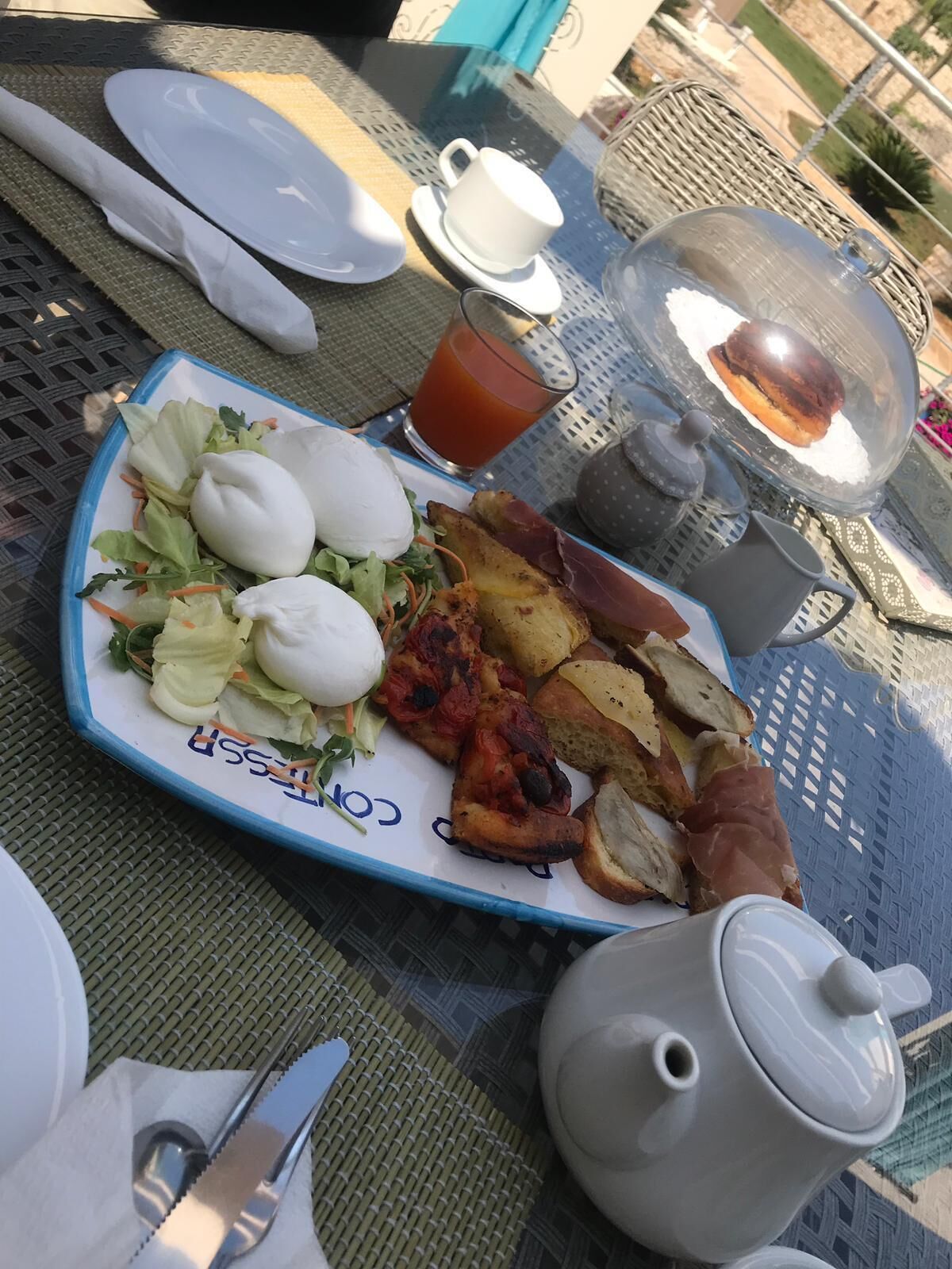 Un tavolo da pranzo con un piatto di cibo, un teiera e un bicchiere di bevanda rossa.