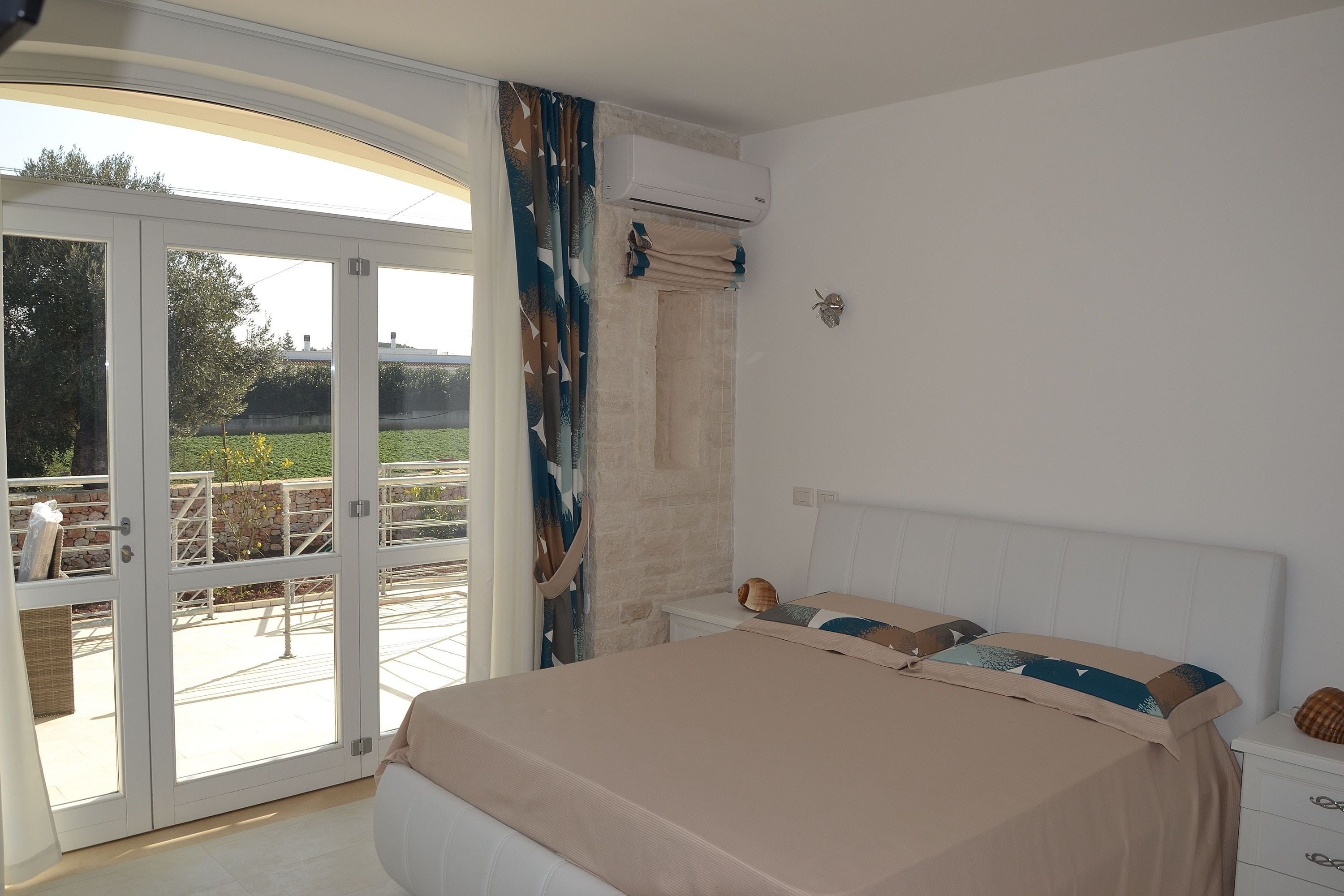 A bedroom with a bed, a nightstand, and a view of a garden through a glass door.
