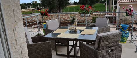 Un patio exterior con una mesa de vidrio, sillas de mimbre y vistas a un paisaje verde.
