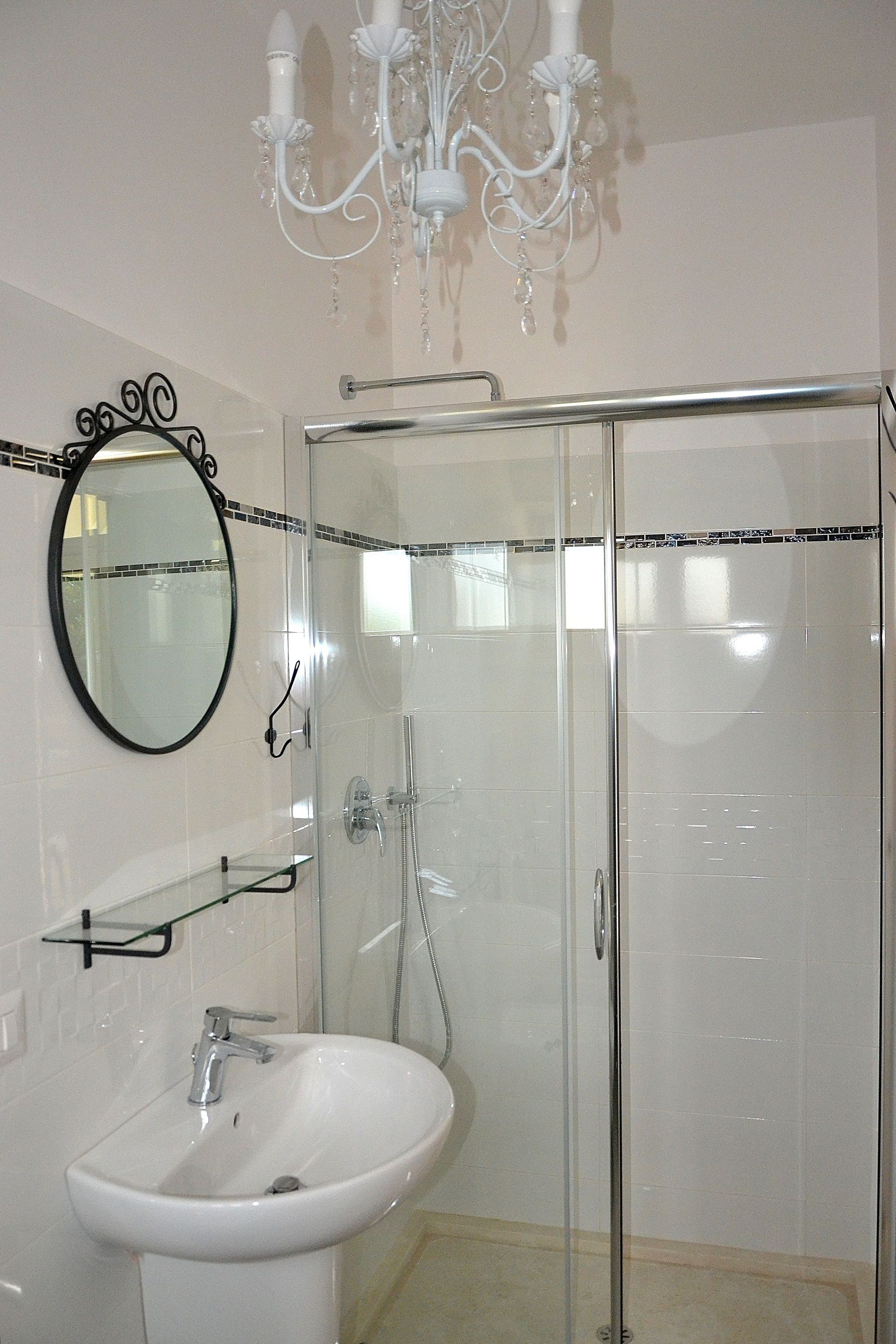 A bathroom with a glass-enclosed shower, a white sink, and a mirror with a black frame.