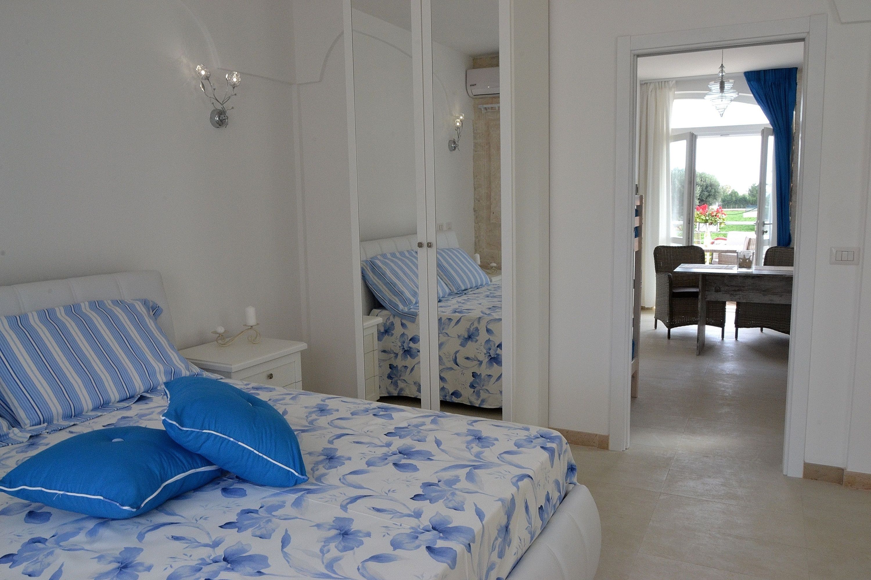 Une chambre à coucher comprenant un lit, une table de chevet, une commode et donnant sur un balcon avec une table et des chaises.