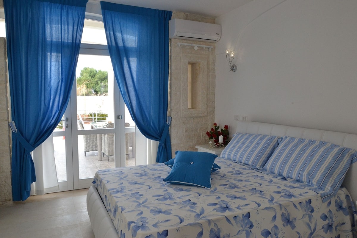 Une chambre à coucher avec un lit, des rideaux bleus, un appareil de climatisation et une vue à travers les portes vitrées.