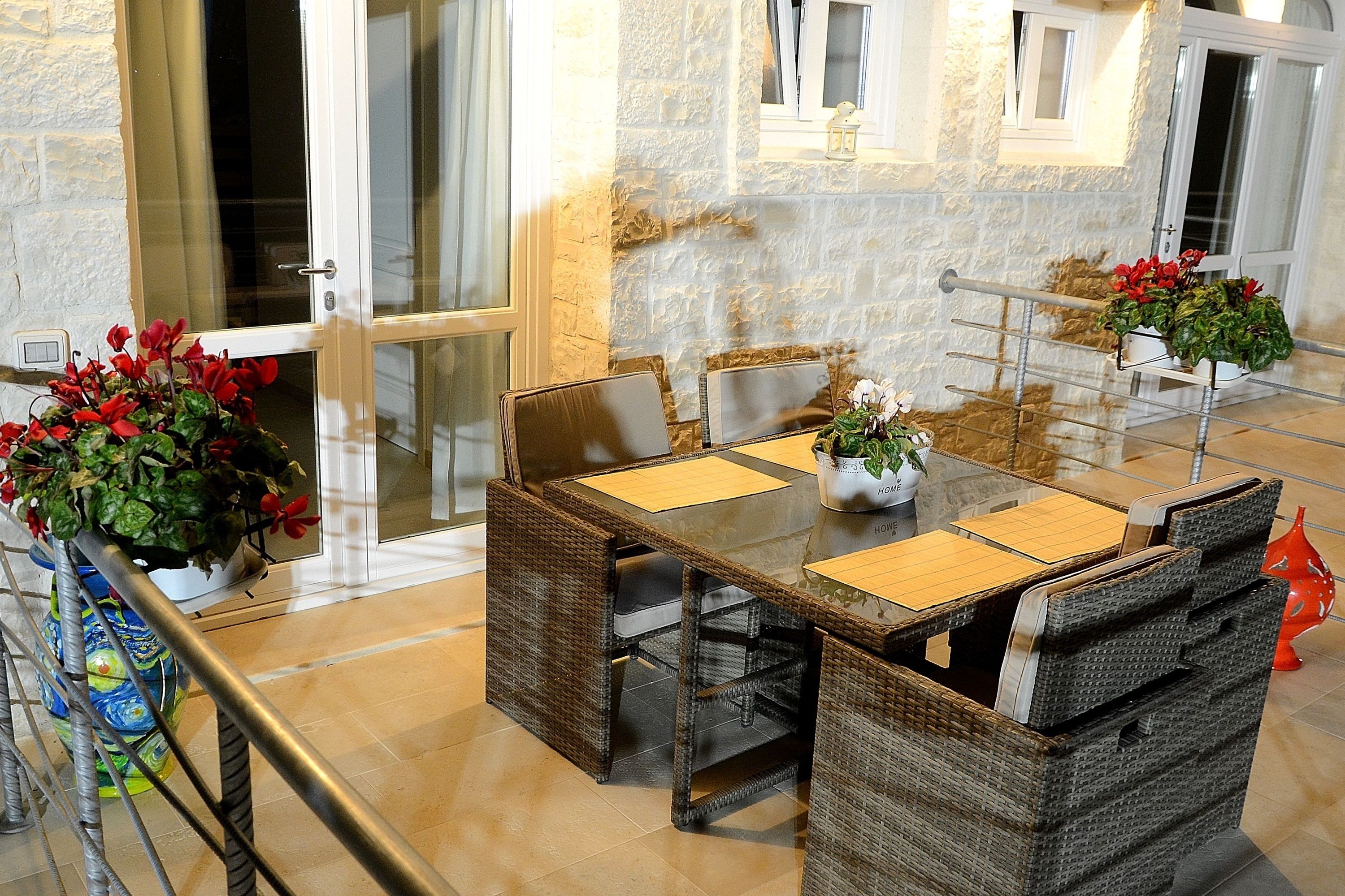 A dining area with wicker furniture, a glass table, and potted plants.