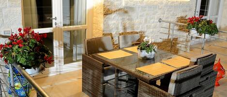 Comedor con mobiliario de mimbre, una mesa de vidrio y plantas en macetas.