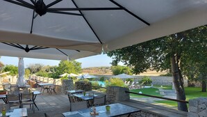 Ein Patio mit Steinsäulen, Tischen, Stühlen und Sonnenschirmen.