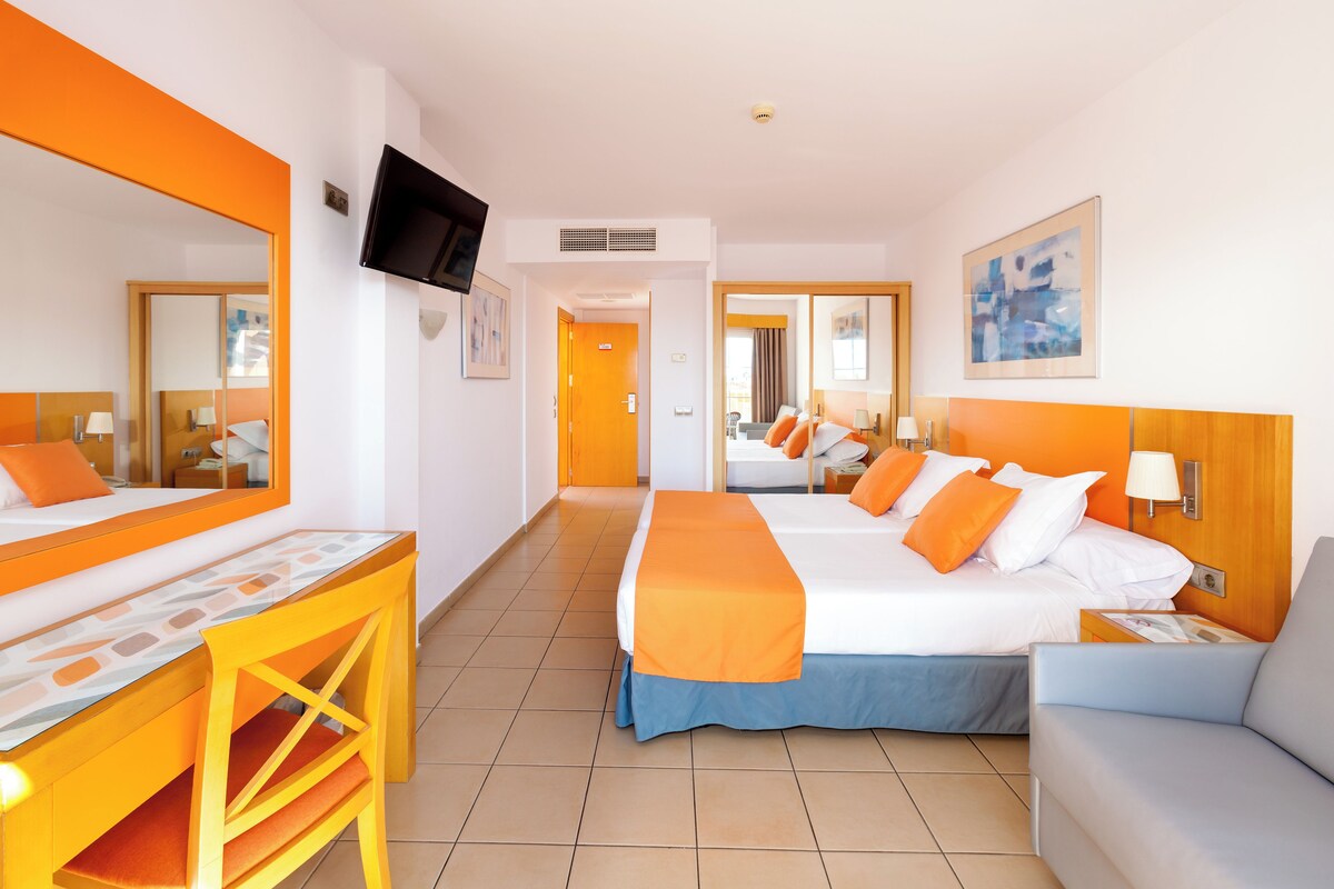 Een hotelkamer met een groot bed, een bureau, een stoel, een televisie en een schilderij aan de muur.