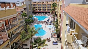 Un hotel con varias piscinas, balcones y palmeras.