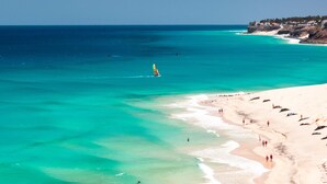 Una playa con aguas turquesas cristalinas, una orilla de arena y un velero a lo lejos.