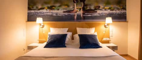 A hotel room with a large bed, two bedside lamps, and a wall-mounted artwork of birds.