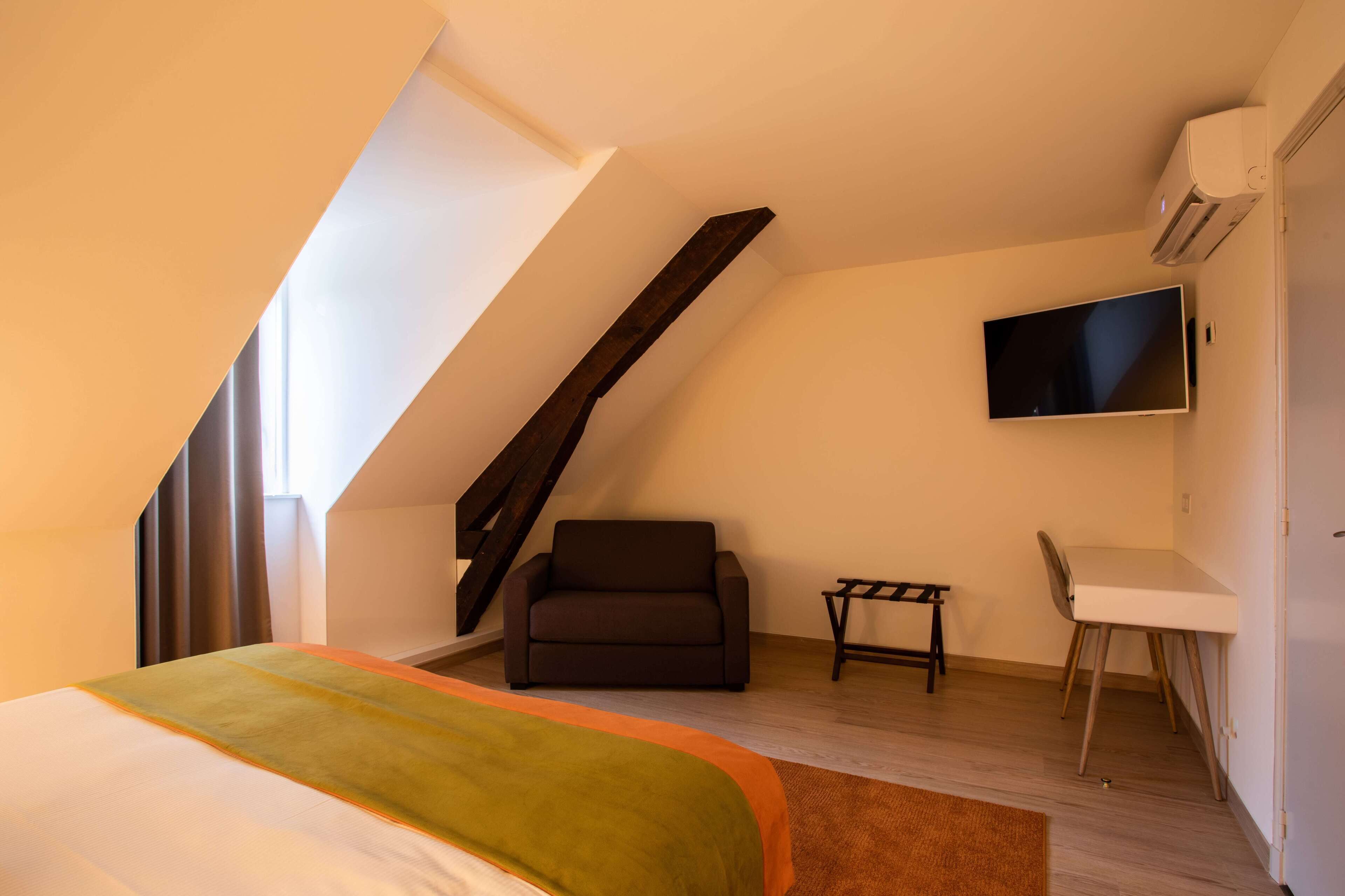 Ein modernes, helles Zimmer mit einem Bett, einer Couch, einem kleinen Tisch und einem an der Wand befestigten Fernseher.
