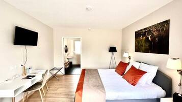 Une chambre d’hôtel équipée d’un lit, d’un bureau, d’une chaise et d’un téléviseur fixé au mur.