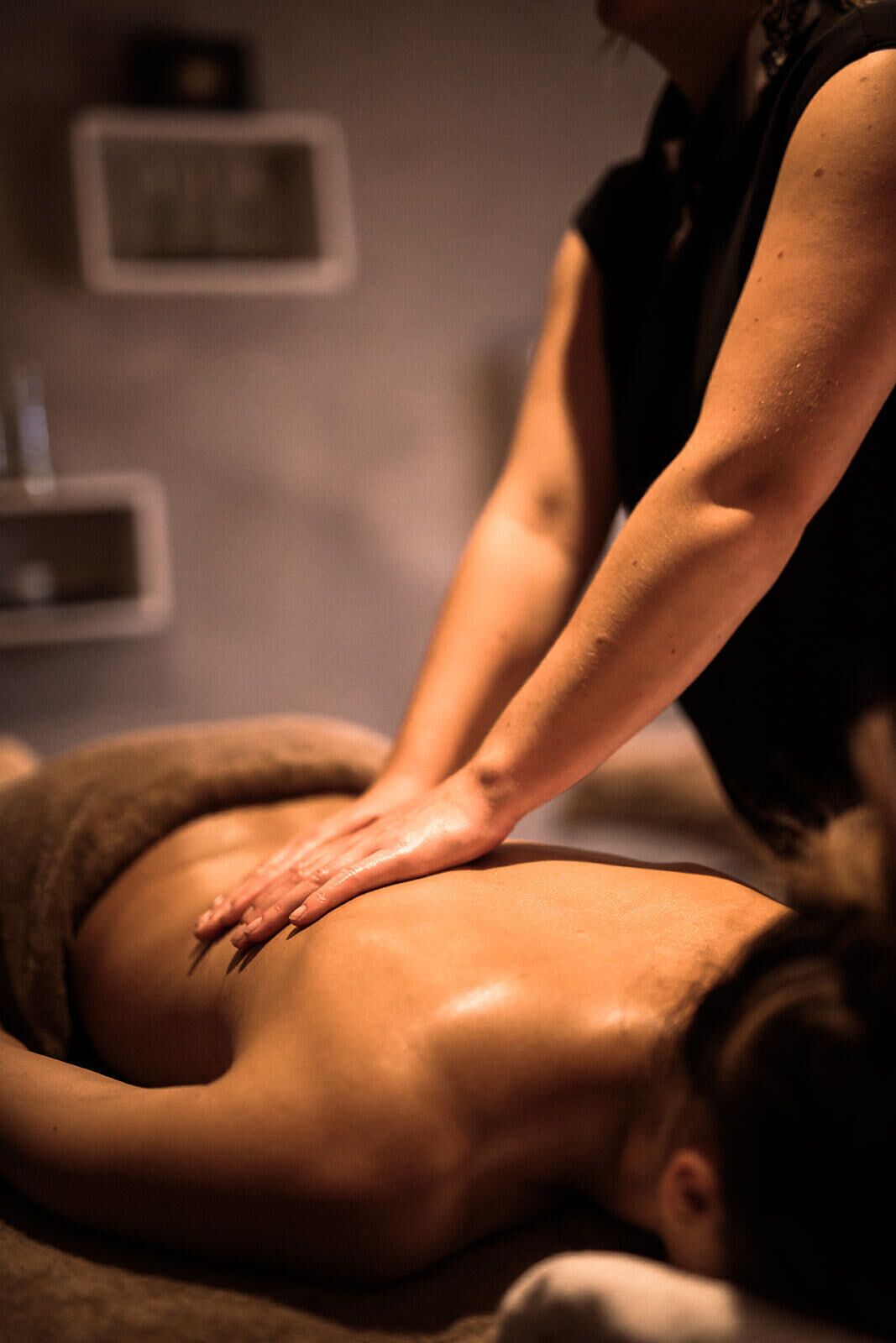 A person receiving a back massage in a room with a massage table and a shelf with items on the wall.