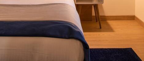 Habitación de hotel con cama, almohadas, mesita de noche con lámpara y un cuadro con aves colgado en la pared.