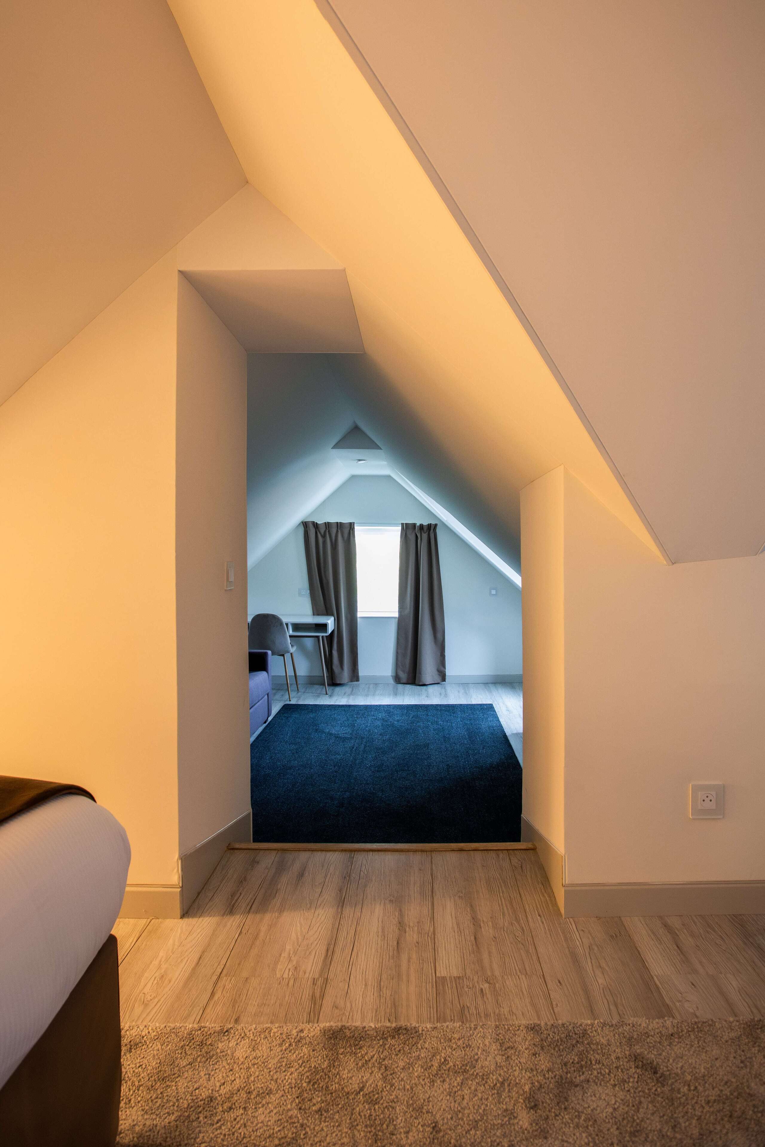 A modern, well-lit attic bedroom with a sloped ceiling, a bed, a desk, and a chair.