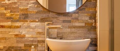 Un baño con pared de piedra, un espejo redondo, un lavabo blanco y una encimera de madera.