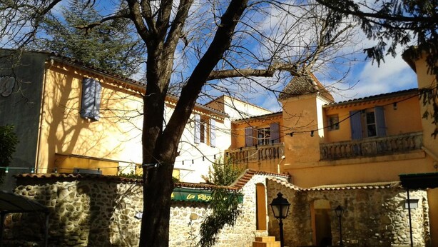 A traditional stone building with a balcony, a tree in the foreground, and a clear blue sky. - Logis Hôtel Le Domaine de la Régalière (Anduze)