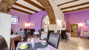 A dining area with tables and chairs, a brick archway, and purple walls. - Logis Hôtel Le Domaine de la Régalière (Anduze)