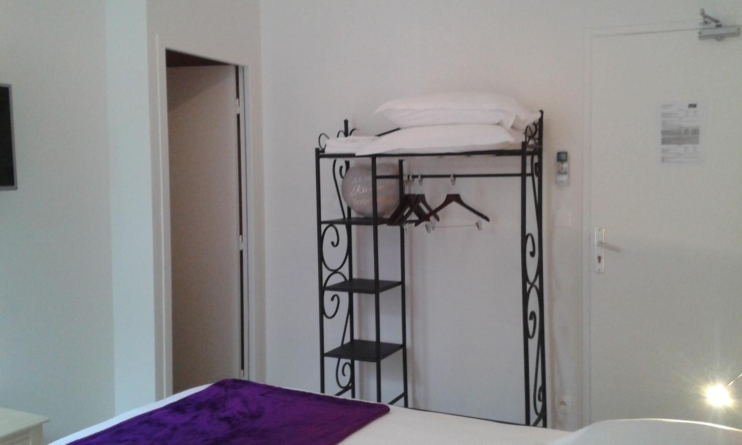 Una habitación con una cama, un armario con repisa y una puerta con interruptor de luz.