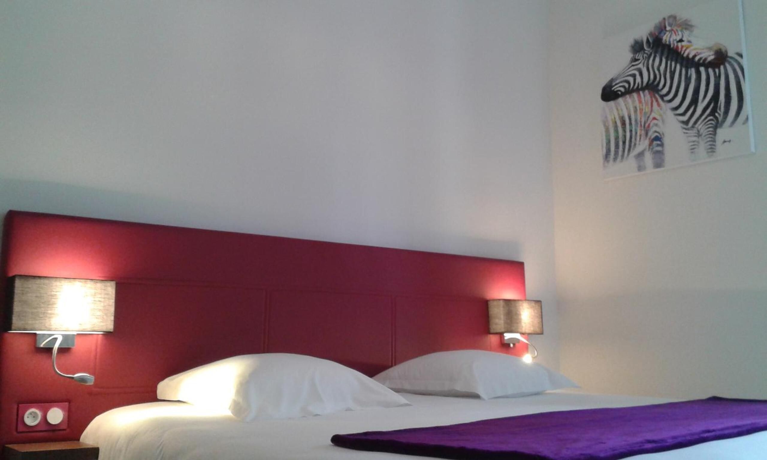 A hotel room with a red headboard, white bedding, and a zebra painting on the wall.