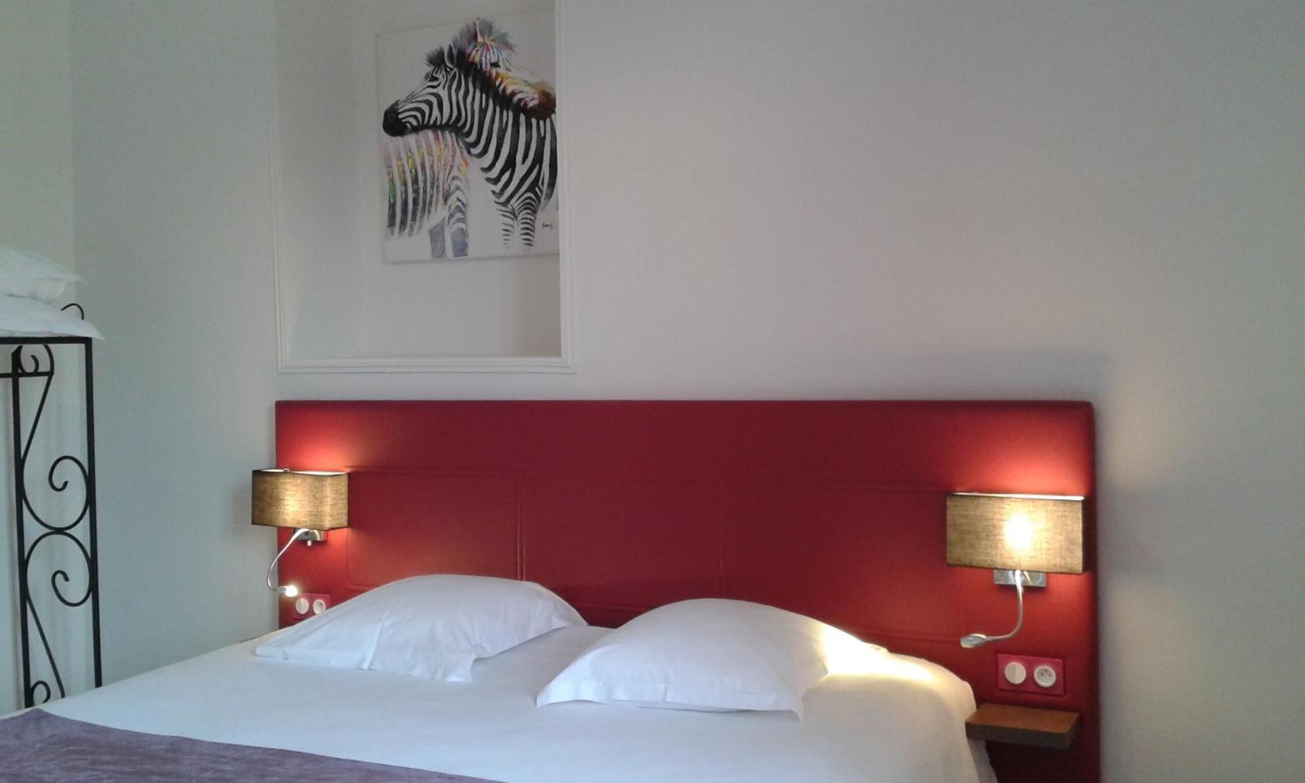 Ein Hotelzimmer mit rotem Kopfteil, zwei Nachttischlampen, einem Zebra-Gemälde an der Wand und einem Bett mit weißen Bettbezügen.