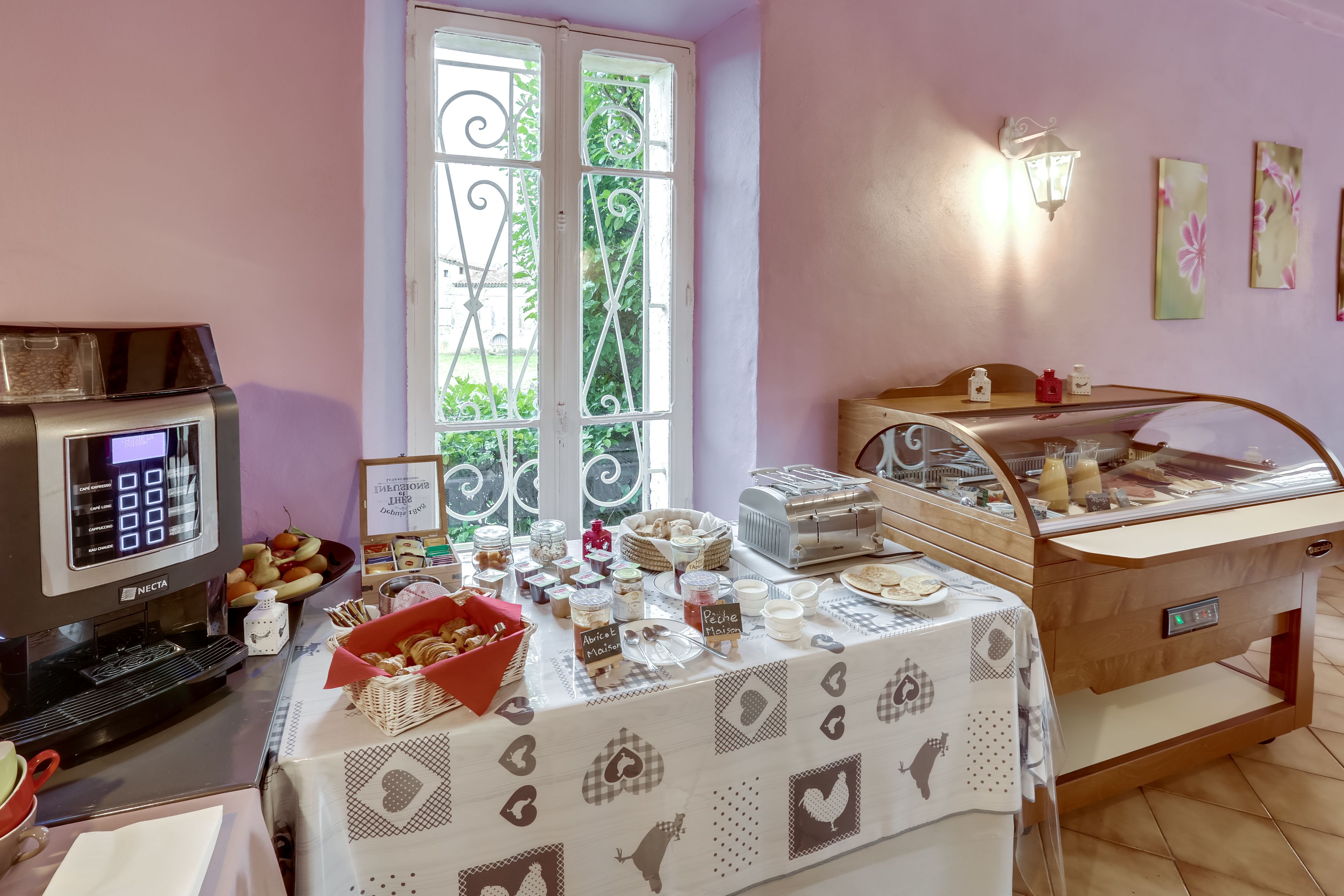 A breakfast buffet setup with a coffee machine, various food items, and a table with a patterned tablecloth.