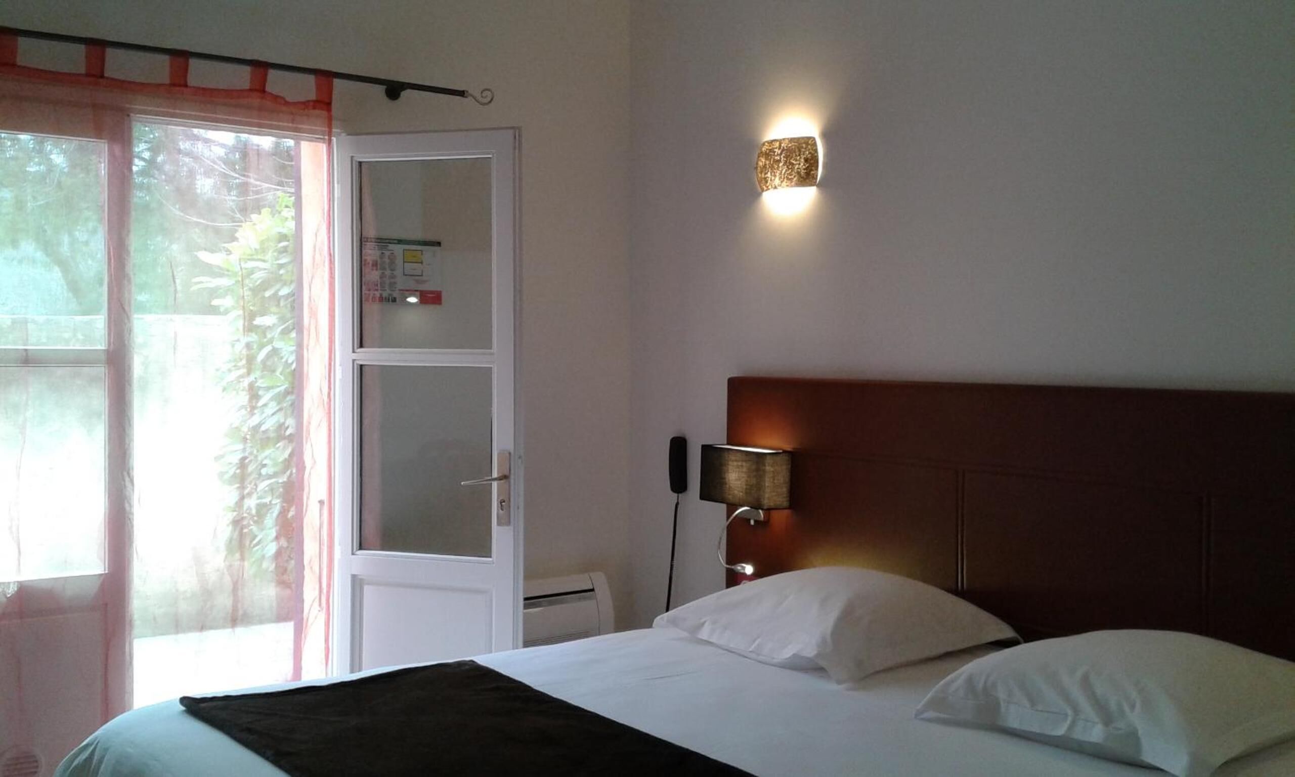 Un dormitorio con una cama, una mesita de noche, una lámpara de pared y una puerta con panel de vidrio esmerilado.