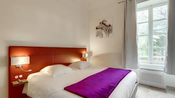 Habitación de hotel con una cama grande, una mesita de noche con lámpara, una ventana con cortinas y una obra de arte colgada en la pared.