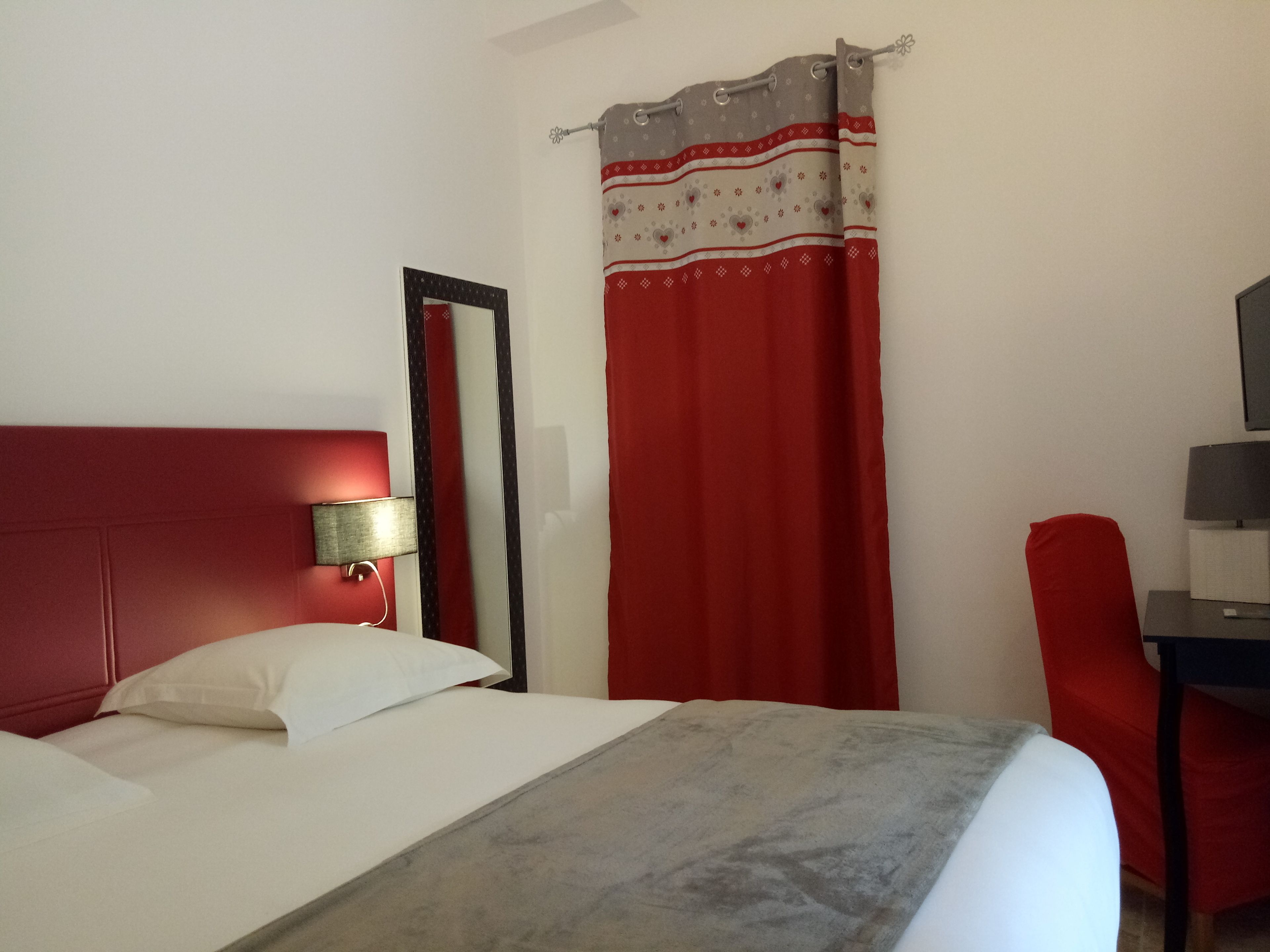 A hotel room with a bed, a desk, a chair, a lamp, and a curtain.