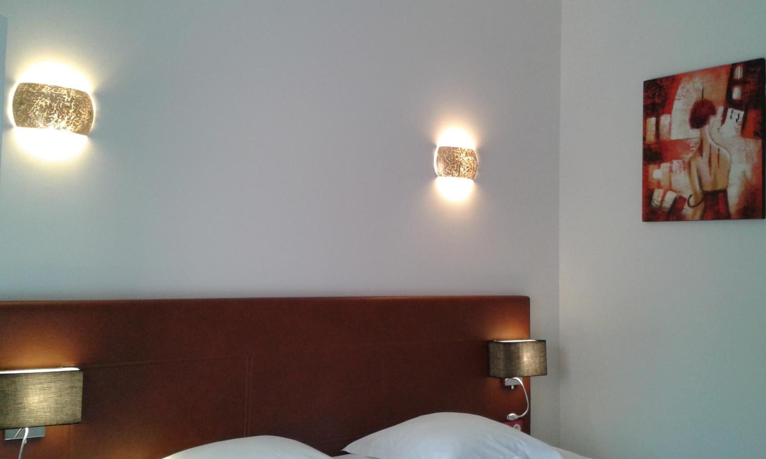 Habitación de hotel con cabecera de madera, dos lámparas de pared y un cuadro.