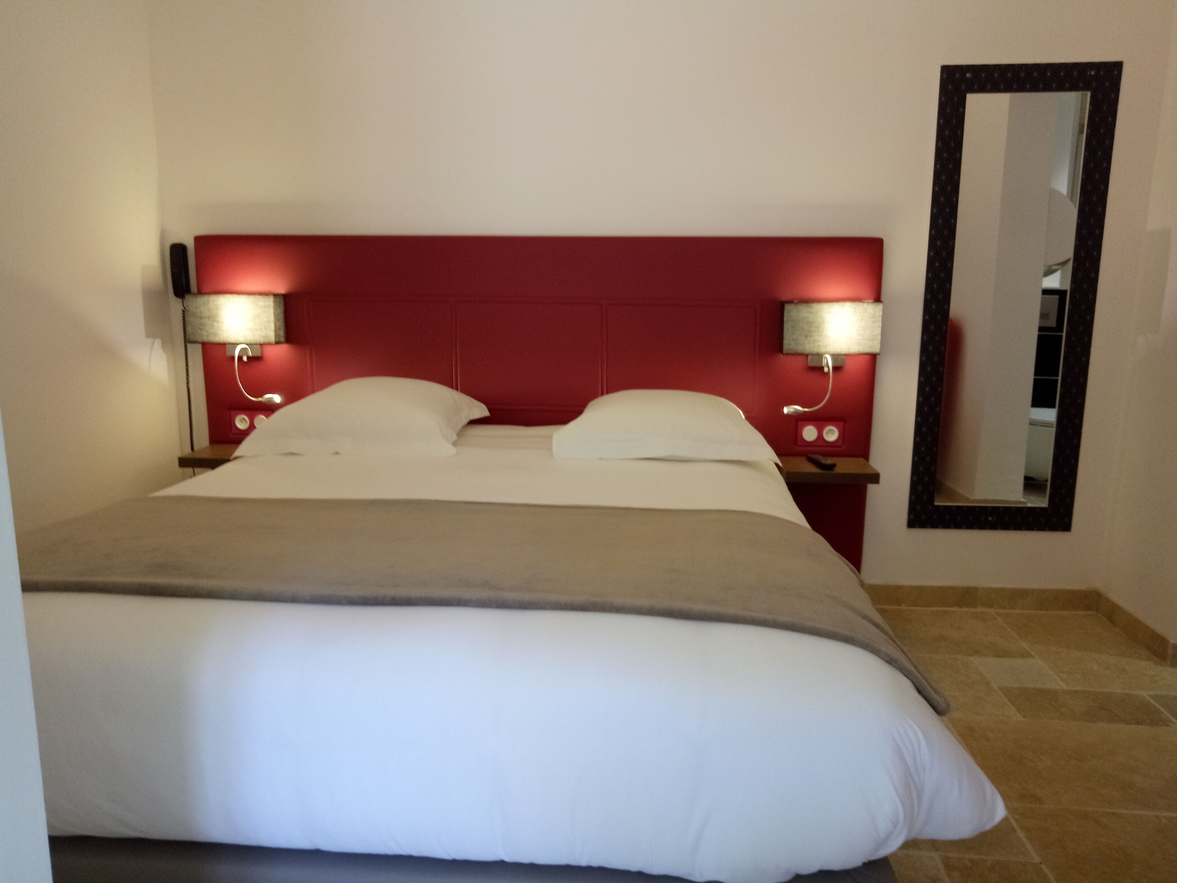 Ein Hotelzimmer mit einem großen Bett, zwei Nachttischen mit Lampen, einem roten Kopfteil und einem Spiegel an der Wand.