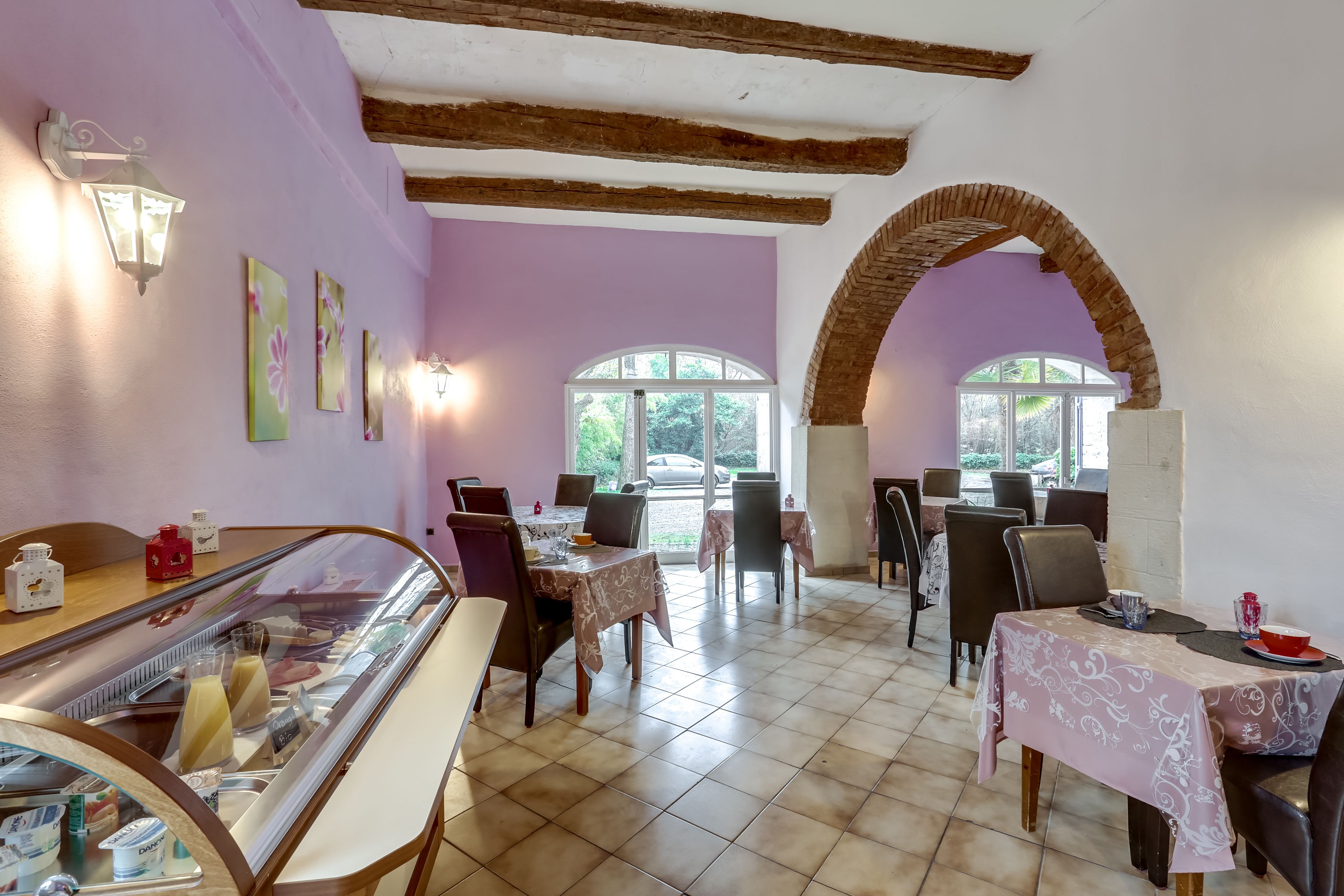 A restaurant with a glass display case, tables with floral tablecloths, and a brick archway.
