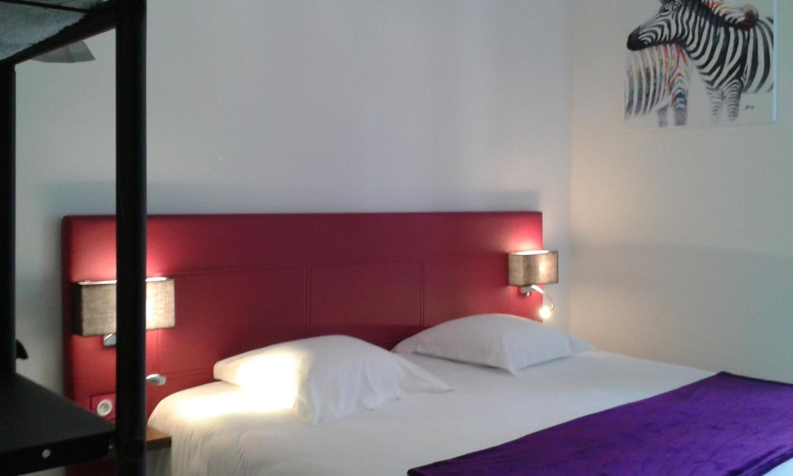 A single-bed room with a red headboard, white bedding, and two wall-mounted lamps.