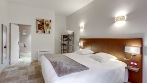 A hotel room with a large bed, a bedside table with a lamp, a wall-mounted light, and a painting. - Logis Hôtel Le Domaine de la Régalière (Anduze)