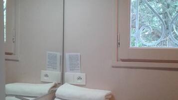 Une salle de bain avec un lavabo blanc, un miroir et une fenêtre ornée d’un cadre en métal décoratif. Deux panneaux sont accrochés au mur, l’un au-dessus du lavabo et l’autre en dessous.