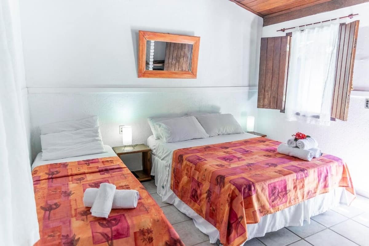 A hotel room with two beds, each with a floral bedspread, a wooden-framed mirror, and a window with curtains.
